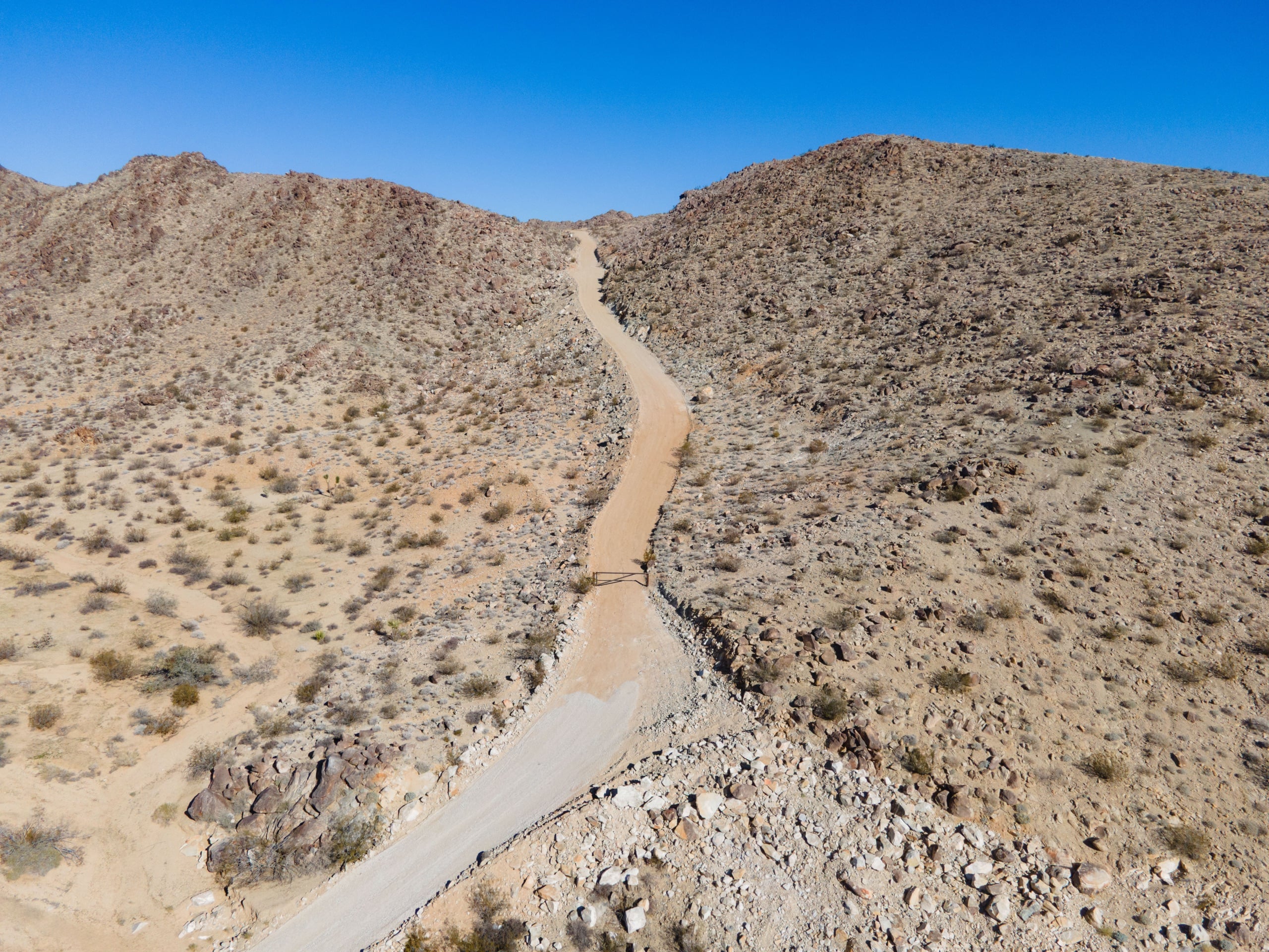 A private dirt road winds through desert hills seen from above