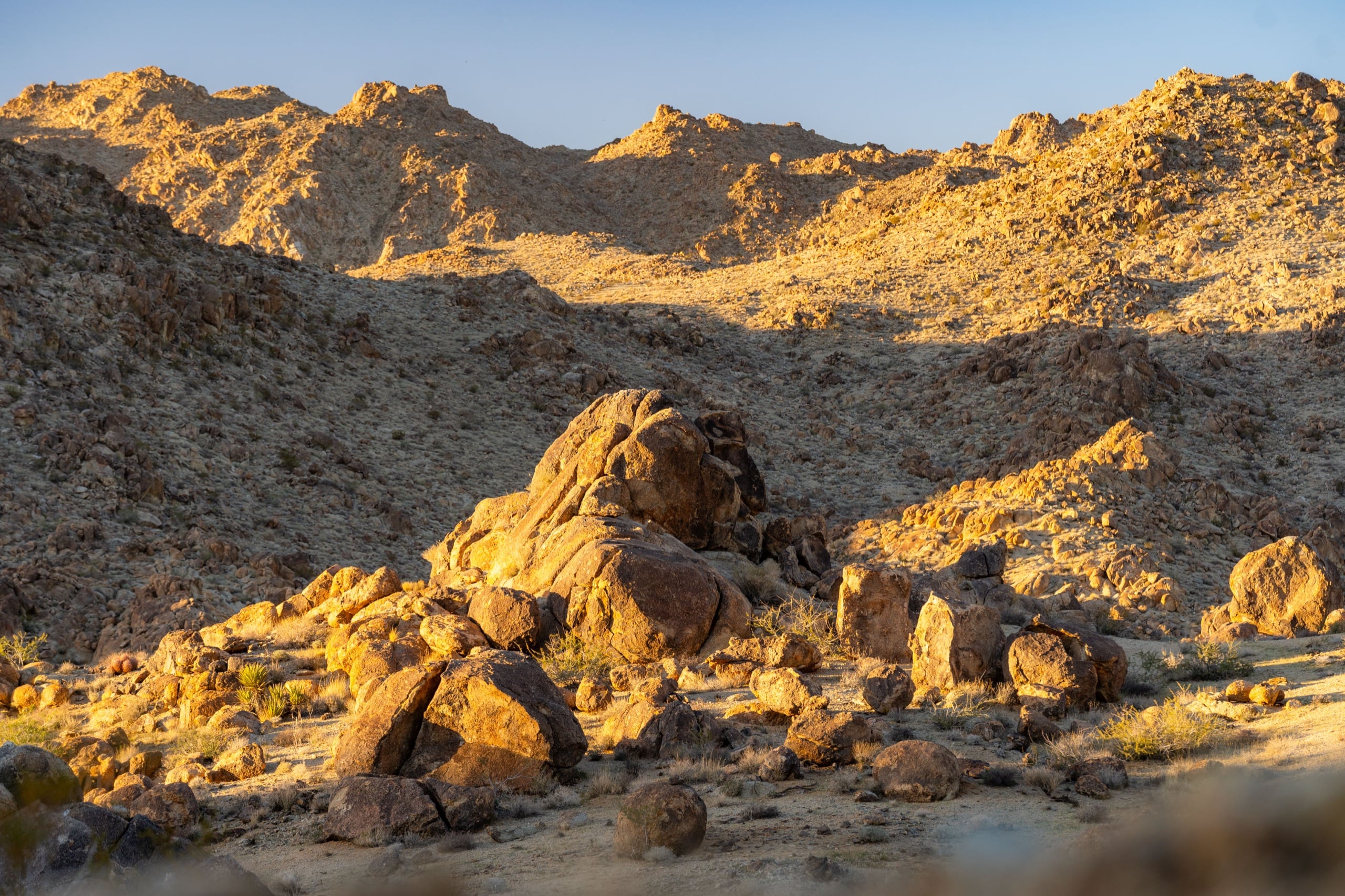 A cluster of granite boulders lit in warm evening light, framed by rocky hills