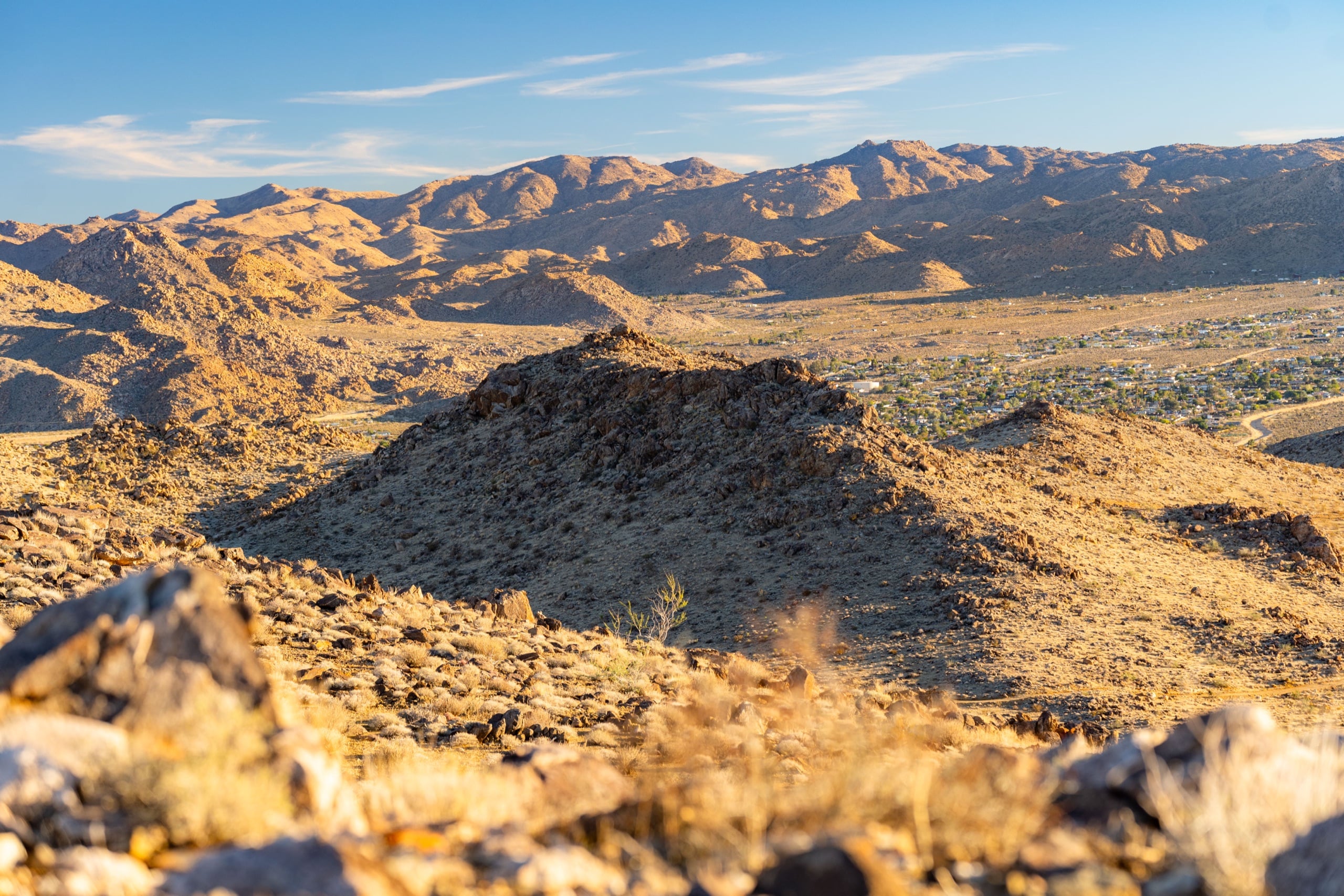 Rolling desert hills bathed in soft evening light, with distant town glimmering below