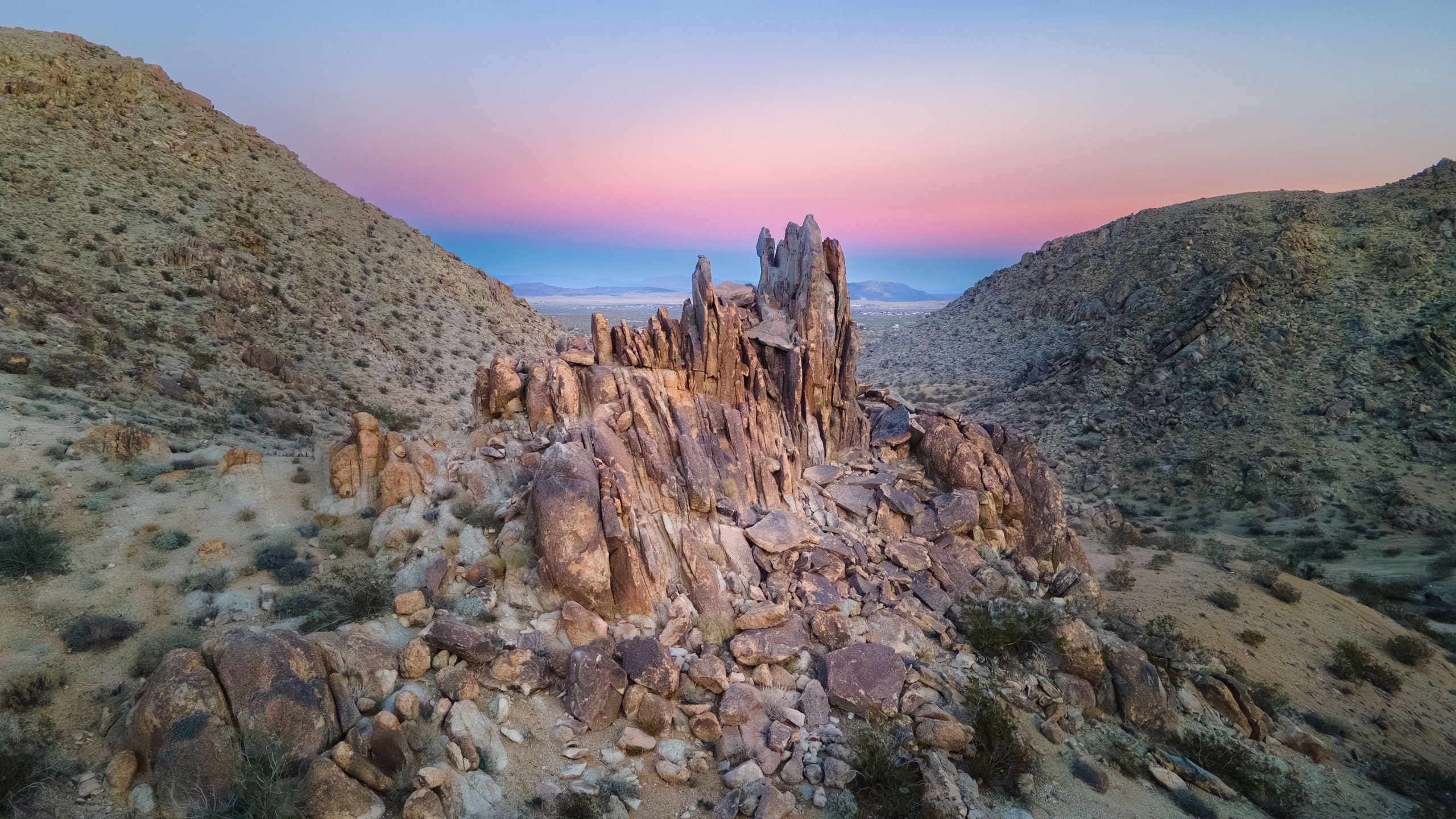 A dramatic rock formation rises against a pink and lavender desert twilight sky